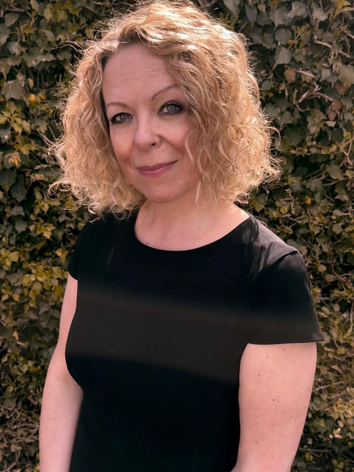 Clare in darker clothing against a calm natural backdrop.