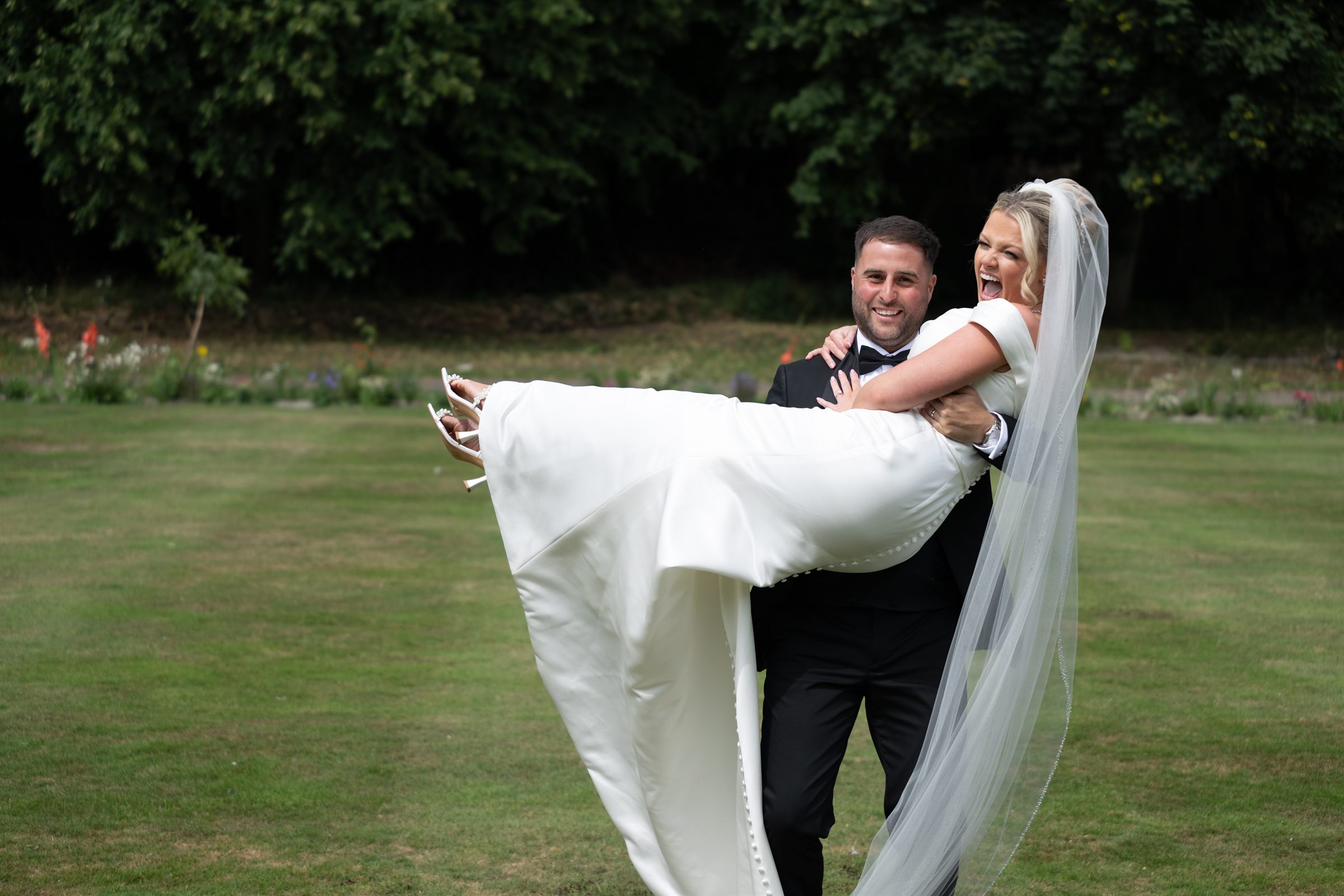 A groom carrying the bride across a lawn after the ceremony.
