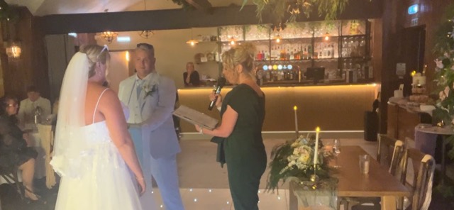Clare holding a microphone and ceremony folder as a bride and groom face one another.