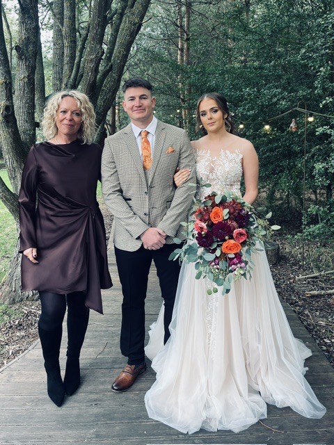 Clare with a wedding couple on a wooden walkway surrounded by trees.